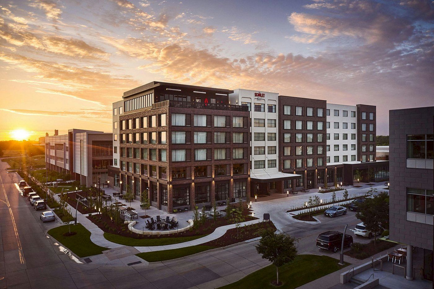 A multi-story hotel building with patios and parking at sunset, with clouds filling the sky.
