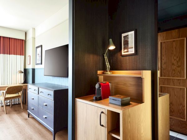 A hotel-style room with a flat-screen TV, cabinet drawers, and a red coffee machine on a wooden counter.
