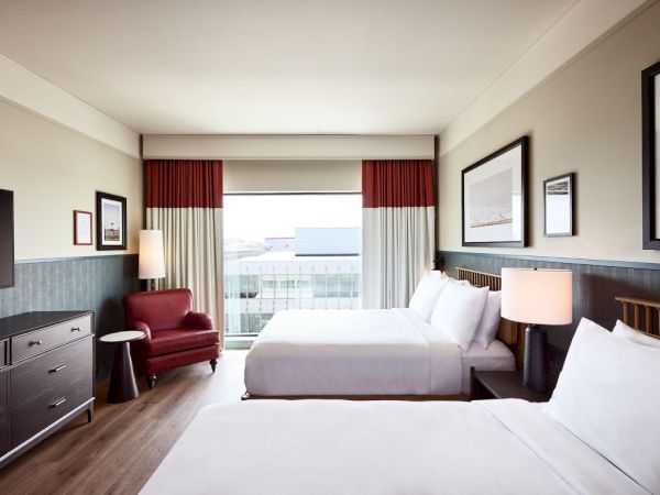A tidy hotel room with two beds, lamps, curtains, and framed wall art.
