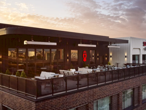 A rooftop terrace with outdoor seating and lighting on a brick building at sunset.