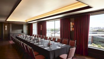 A formal conference room with a long table set for a meeting, red curtains, and warm ceiling lighting.