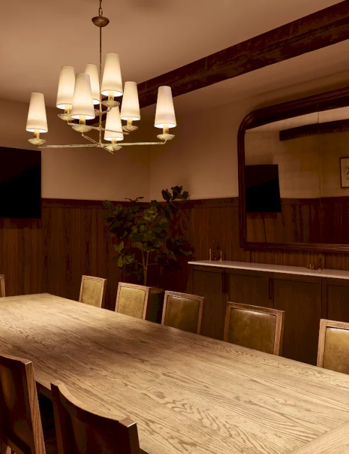 A warm dining room with a long wooden table, cushioned chairs, and hanging chandeliers above paneled walls.