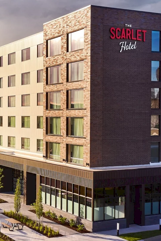 A modern hotel building labeled &ldquo;The Scarlet Hotel&rdquo; with outdoor seating and landscaped walkways along the front.