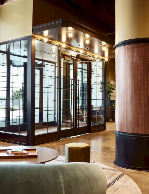 Modern office lobby lounge with glass partitions, warm lighting, and tall wood cylindrical columns.