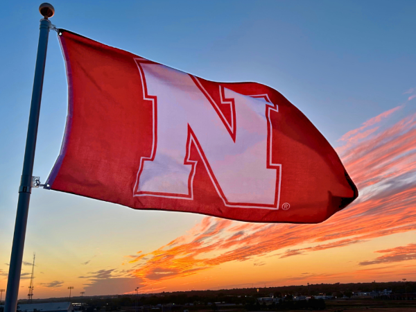 A large red flag with a white &ldquo;K&rdquo; waves at sunset over a parking lot full of cars.