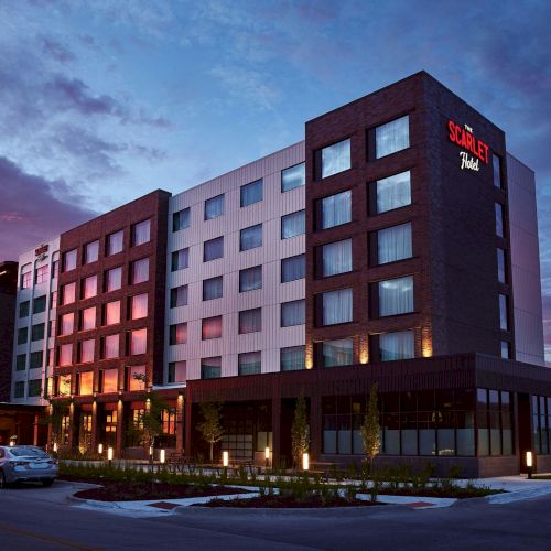 A modern hotel building with &ldquo;The Scarlet Hotel&rdquo; signage glowing at dusk under a colorful sky.