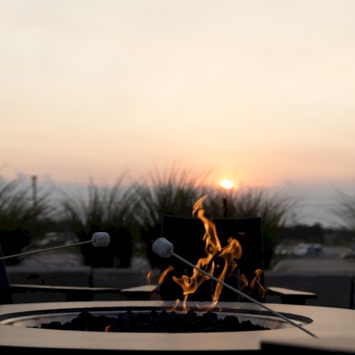 A sunset over a backyard fire pit where marshmallows roast on skewers, with flames flickering in the foreground.