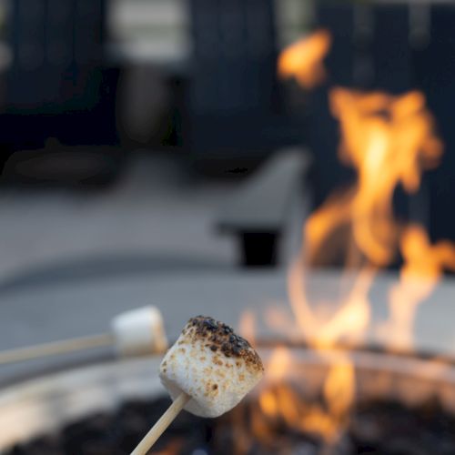 A toasted marshmallow on a stick roasting over an open campfire beside dark rocks.
