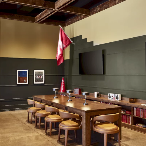 A meeting room with a long wooden table, chairs, books, a red flag, and framed pictures under wooden beams.