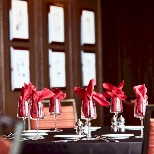 A formal dining table set with crystal glasses, silverware, and red bow-tied napkins in warm daylight.