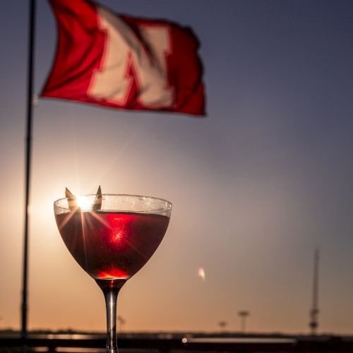 A red wine cocktail in a stemmed glass sits at sunset while a red, white, and blue flag waves above it.