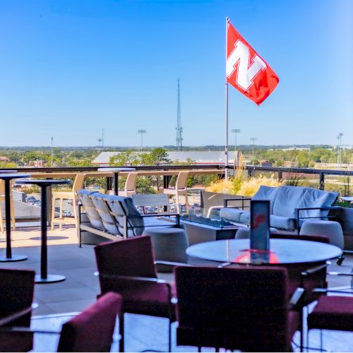 An outdoor patio with lounge chairs overlooks a facility while a red-and-white flag waves above the skyline in daylight.
