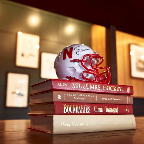 A football helmet sits on top of stacked books, glowing under warm lights in a cozy room setting.